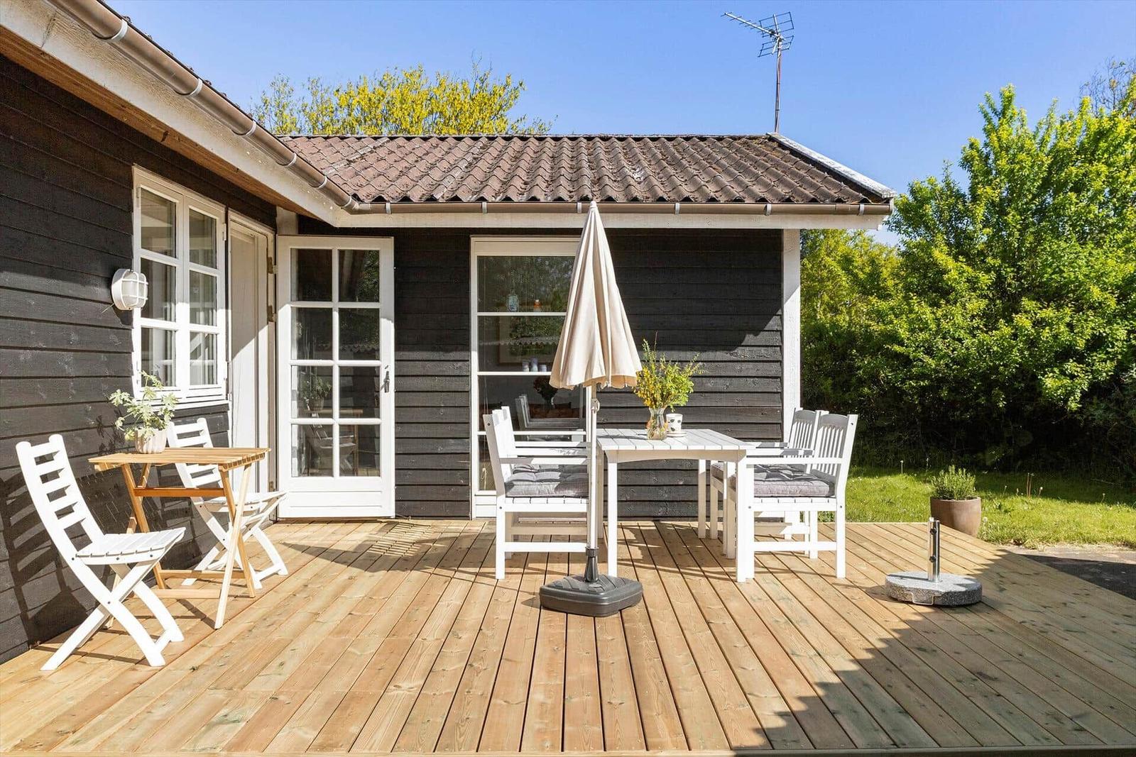 Terrasse mit Tisch, Stühlen und Sonnenschirm. Holzdecke, Fenster und Garten.