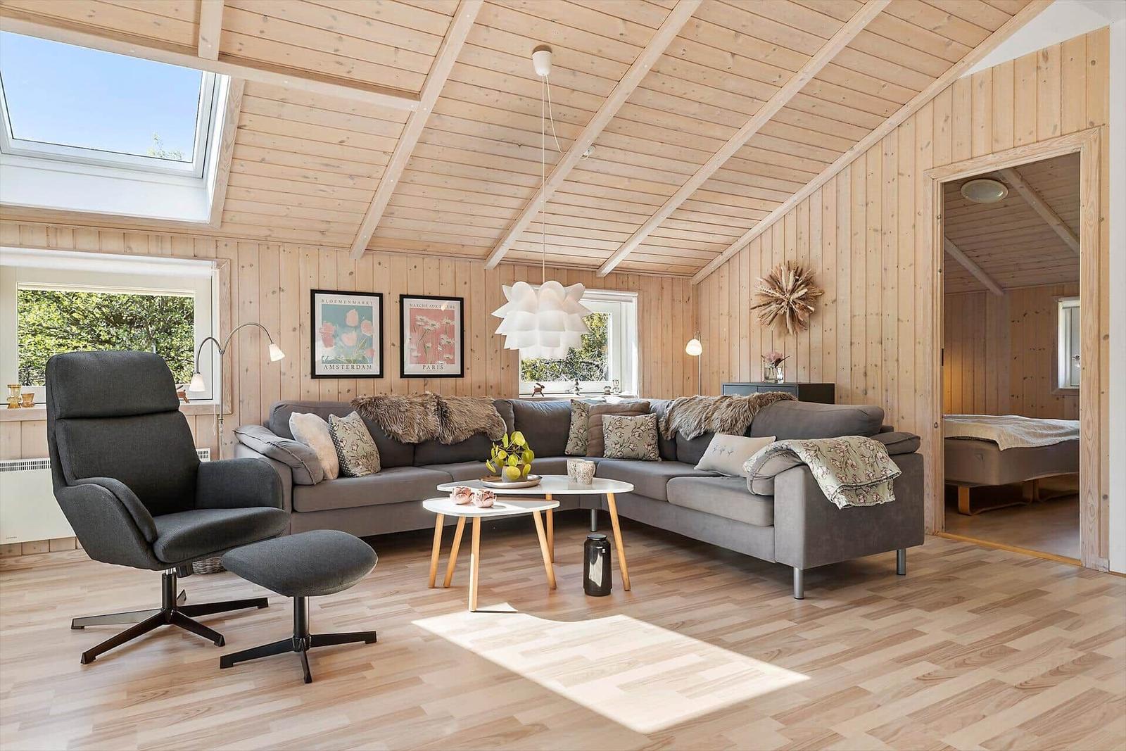 Wohnraum mit Holzwand, Sofa, Sessel und Blick auf Schlafzimmer.