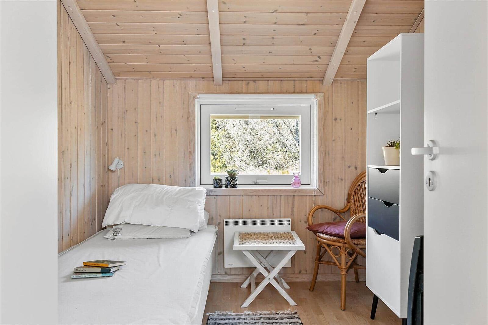 Ein Schlafzimmer mit Bett, Stuhl und Fenster. Holzwände und Decke.
