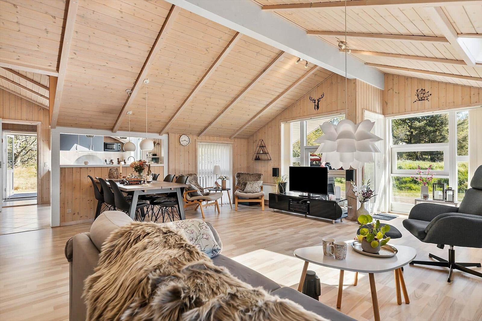 Wohnbereich mit Essbereich und Küche unter Holzdecke. Große Fenster und moderne Möbel.