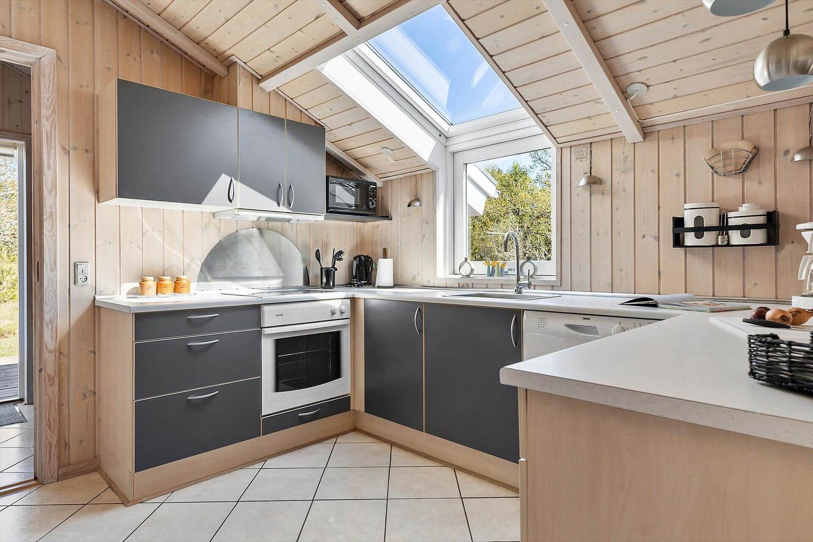 Küche mit Holzwänden, grauen Schränken und Dachfenster. Weiße Arbeitsplatten und moderne Geräte.