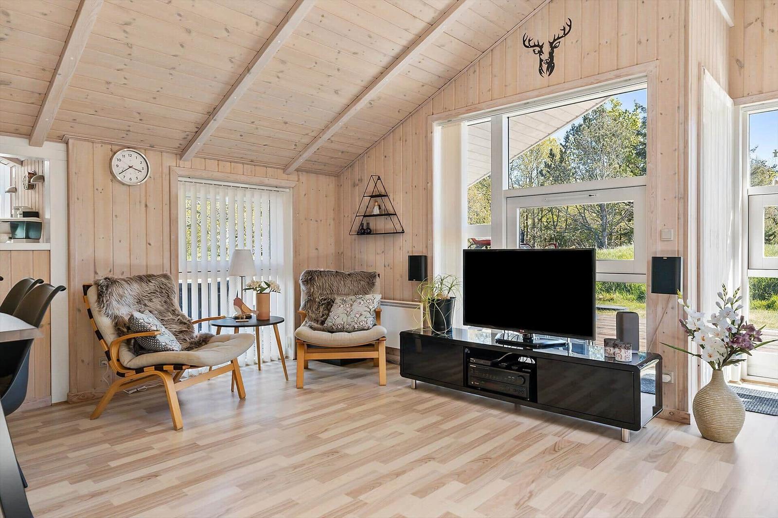 Wohnzimmer mit Holzwand, TV, zwei Sessel und großem Fenster zur Außenseite.