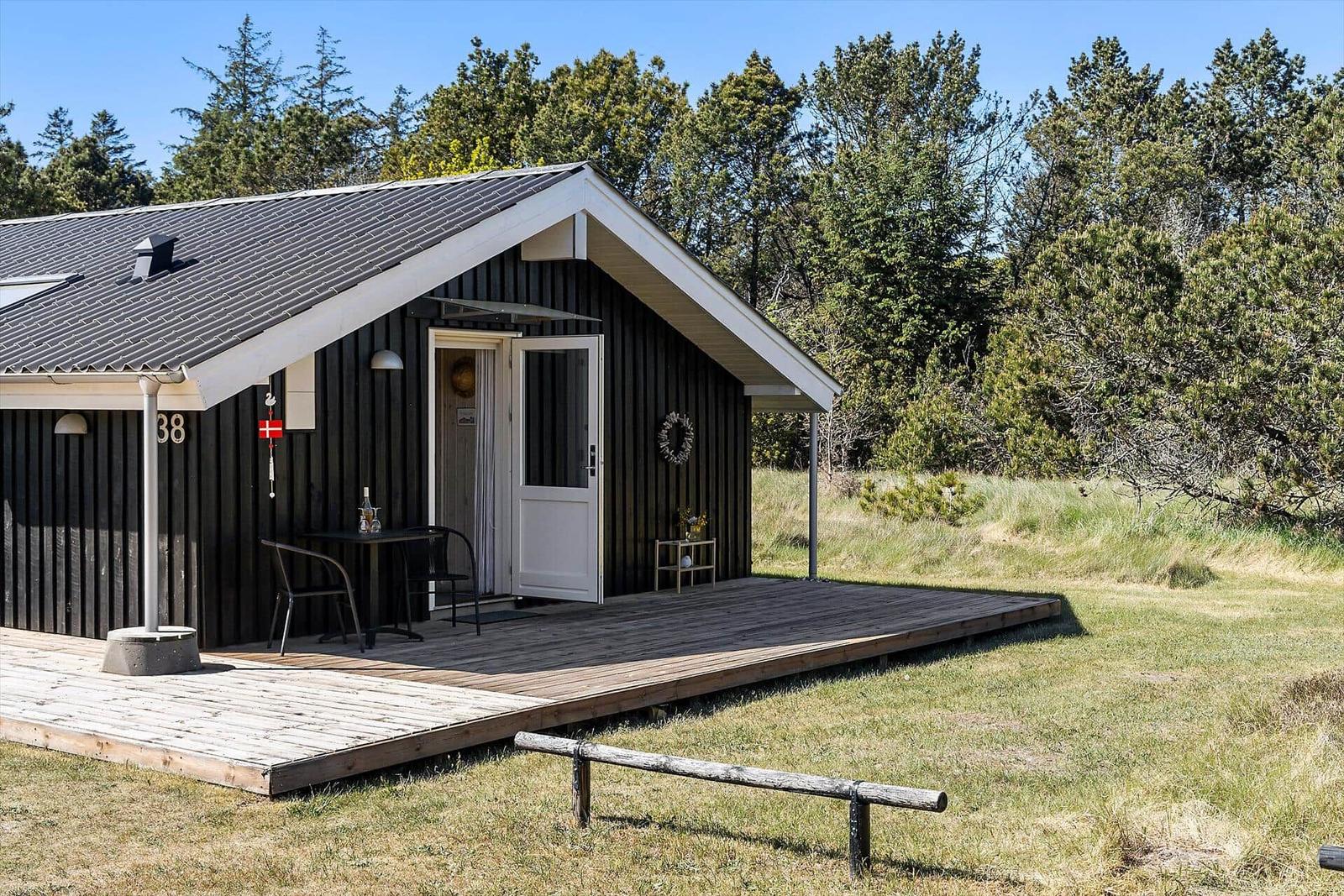 Hütte mit Holzterrasse und Garten. Tür mit Fenster und kleine Tischbank.