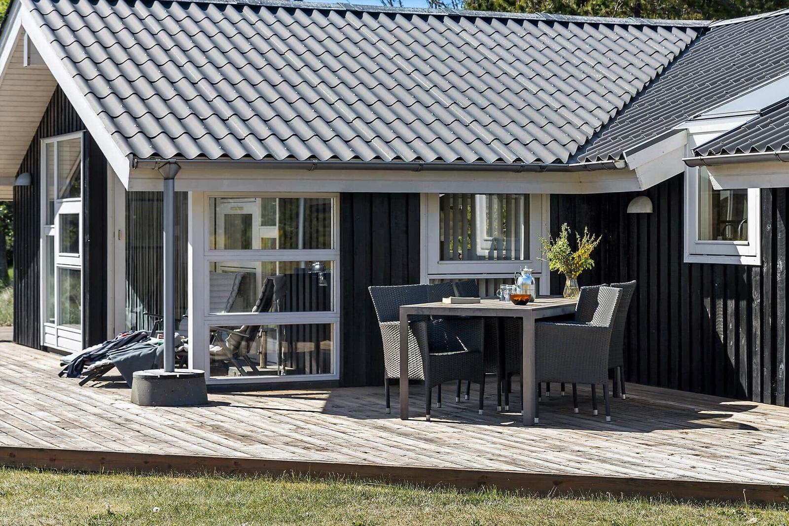 Terrasse mit Tisch und Stühlen vor einem Haus mit dunkler Fassade und grauem Dach.