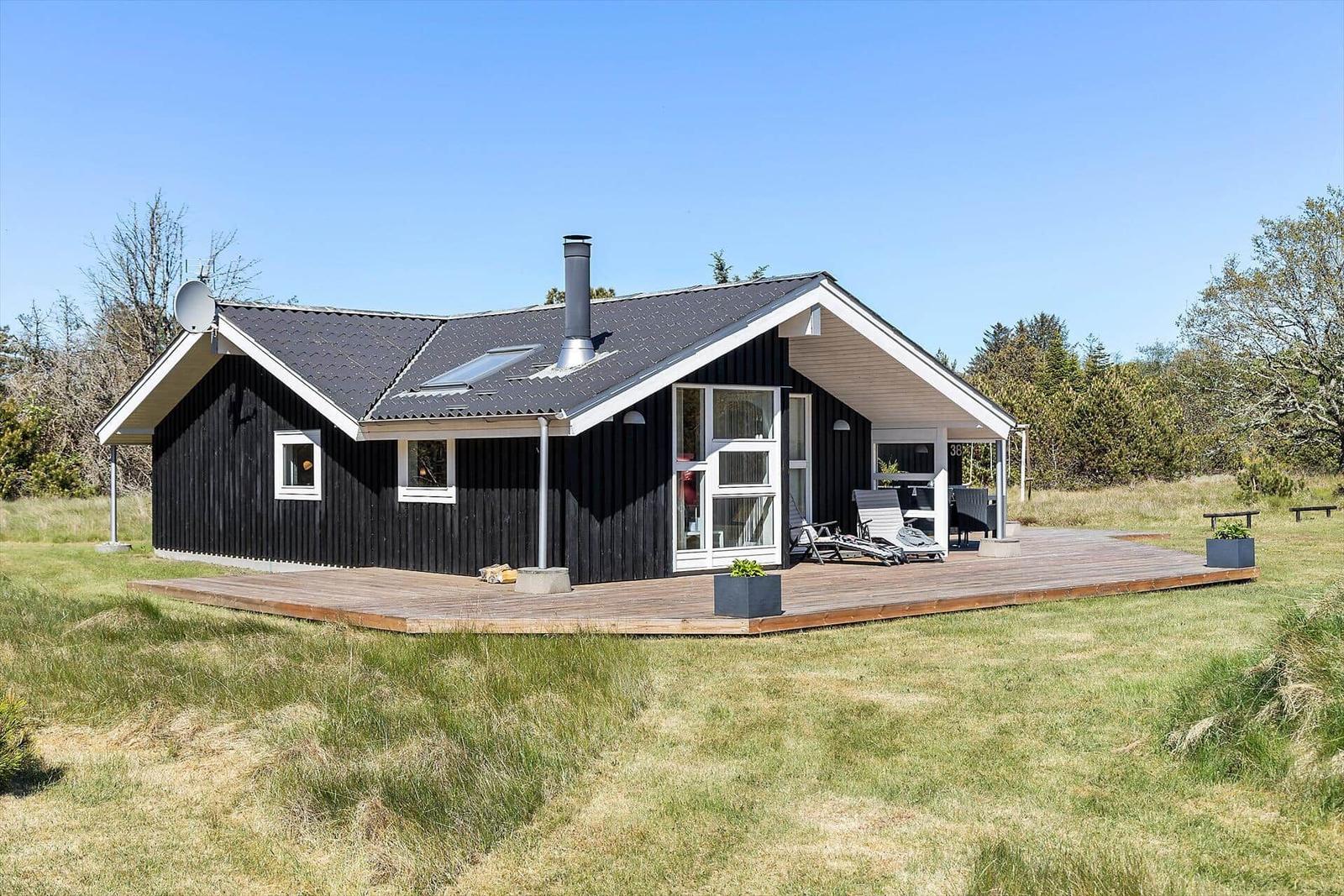 Schwarzes Holzhaus mit Terrasse und Garten. Außenbereich mit Liegen und Pflanzen.