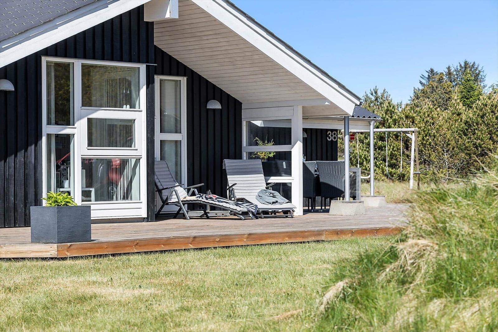 Haus mit Terrasse, Liegen und Garten. Nummer 38. Hintergrund mit Bäumen.