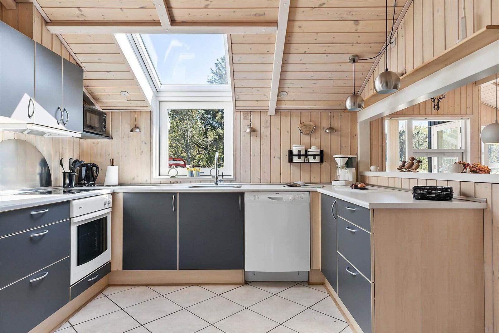 Küche mit Holzwand, grauen Schränken und Fenster. Dachfenster, Spüle, Kochfeld und Waschmaschine.
