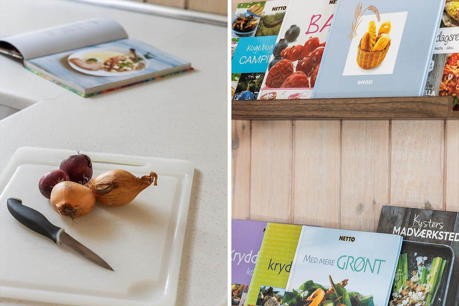 Küchenarbeitsfläche mit Schneidebrett, Knoblauch und Kochbuch. Regal mit Kochbüchern an Holzwand.