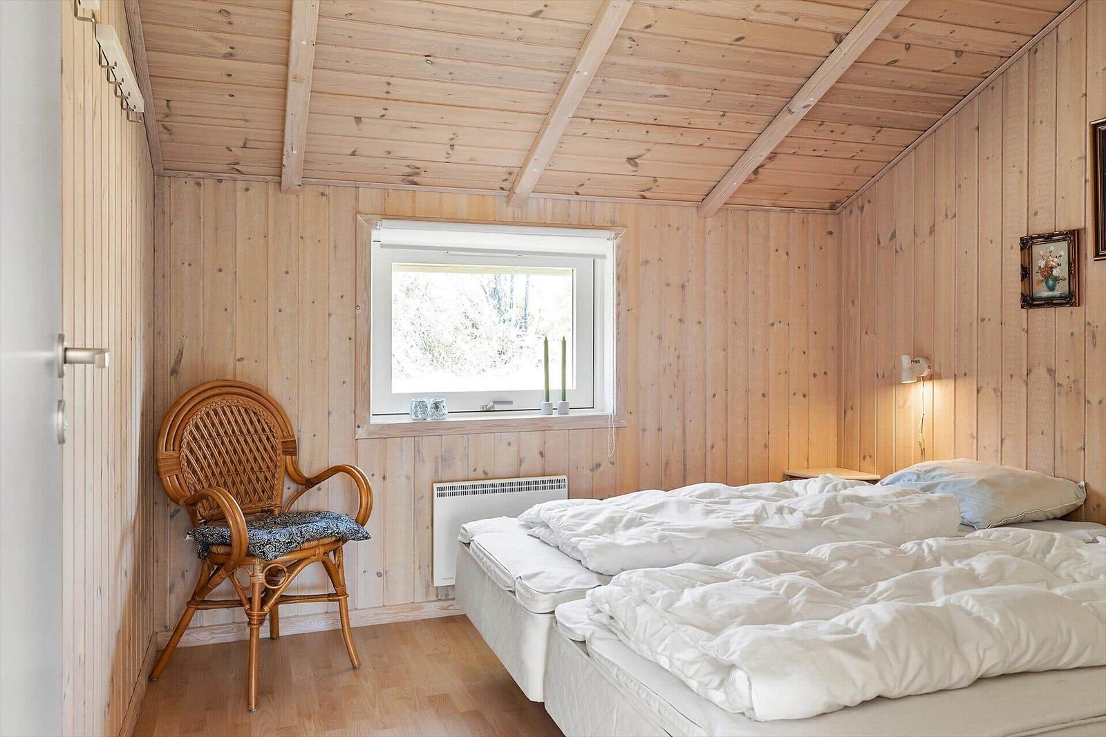 Schlafzimmer mit Holzwand, Bett, Stuhl und Fenster