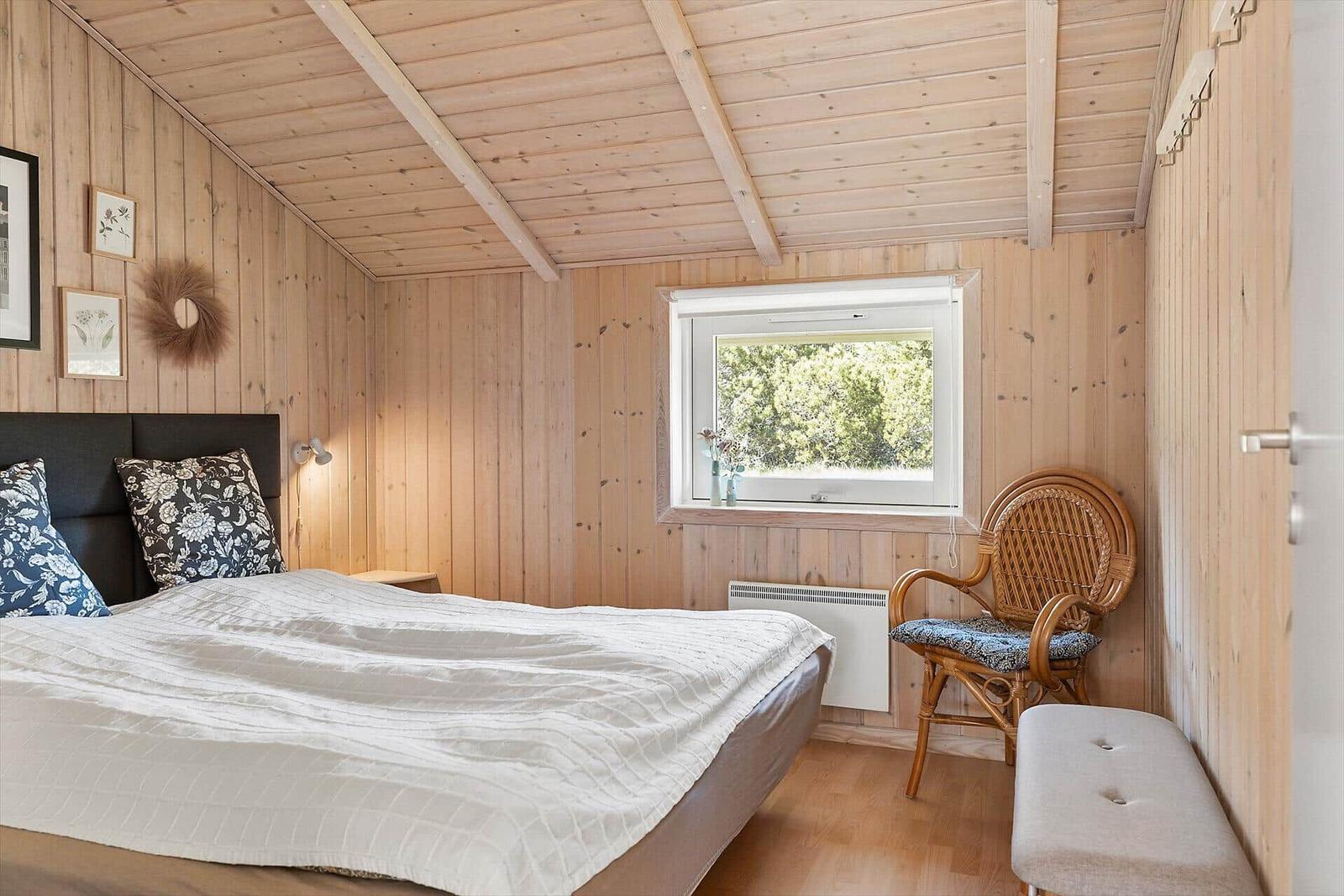 Schlafzimmer mit Holzwänden, Bett, Stuhl und Fenster.