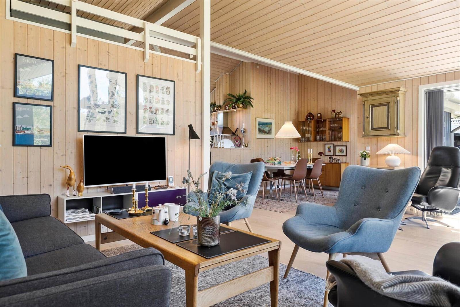 Living and dining area with wooden walls, blue chairs, and TV.