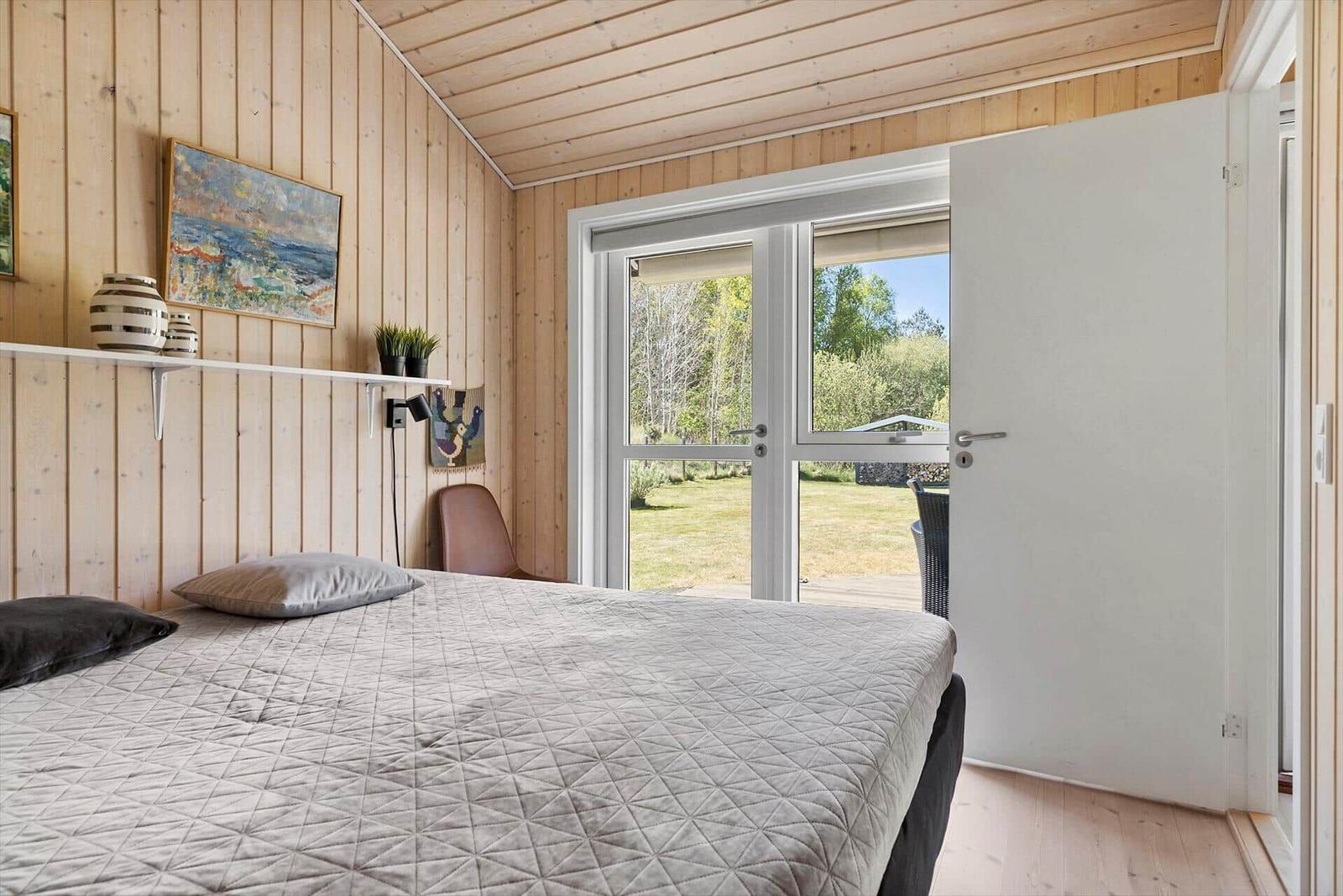 Bedroom with wooden walls, bed, and window to terrace.