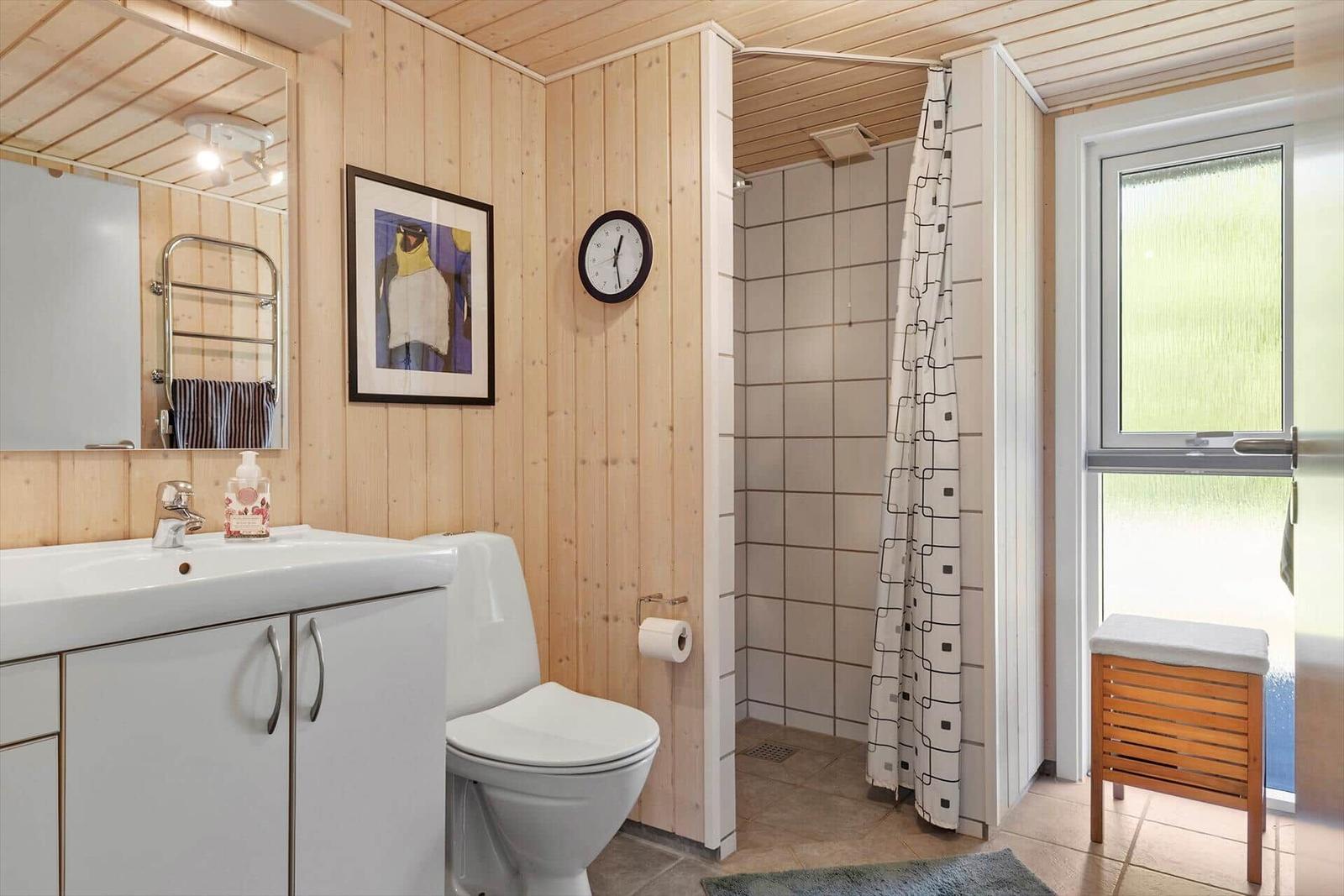 Bathroom with shower, toilet, and sink. Wooden walls and window with view.