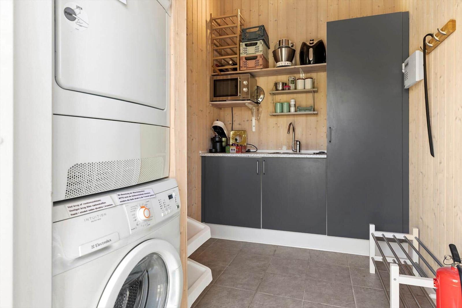 Washing machine and dryer in a small kitchen with wooden walls and gray cabinets.