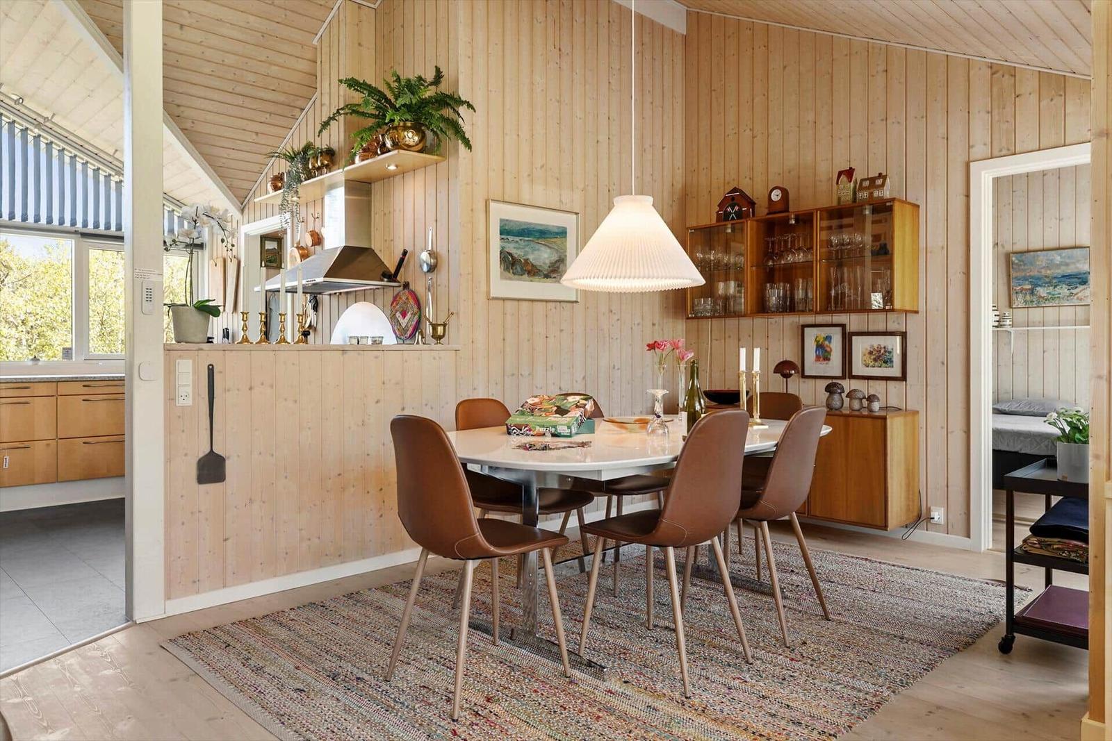 Dining area with table, chairs, and wooden walls. Kitchen and bedroom are visible.