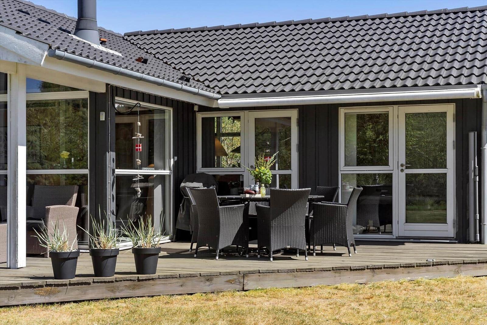 Deck with seating and plants in front of a house with dark wood and roof