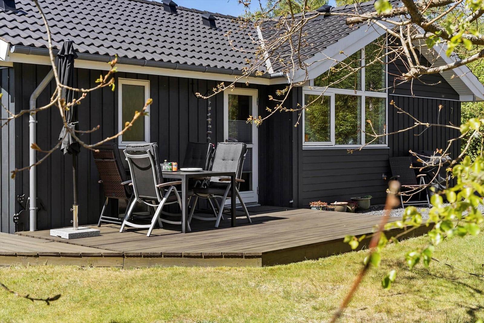 Deck with table and chairs in front of a house with dark siding.