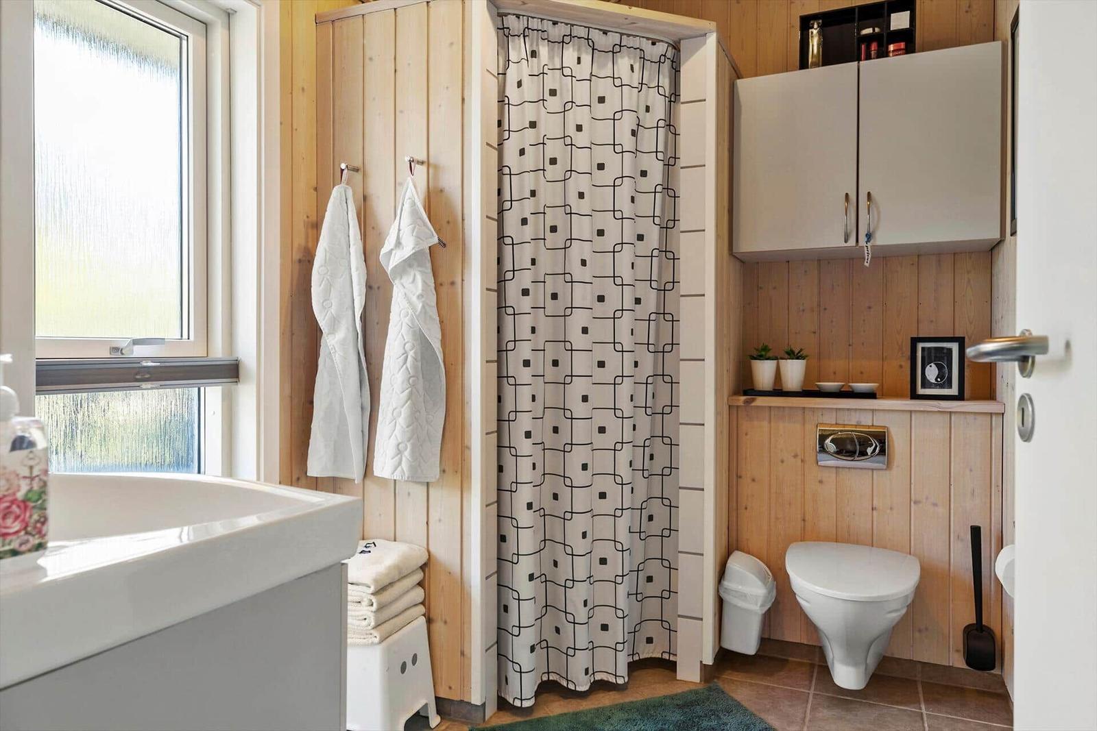 Bathroom with shower, toilet, and sink. Wooden walls and window.