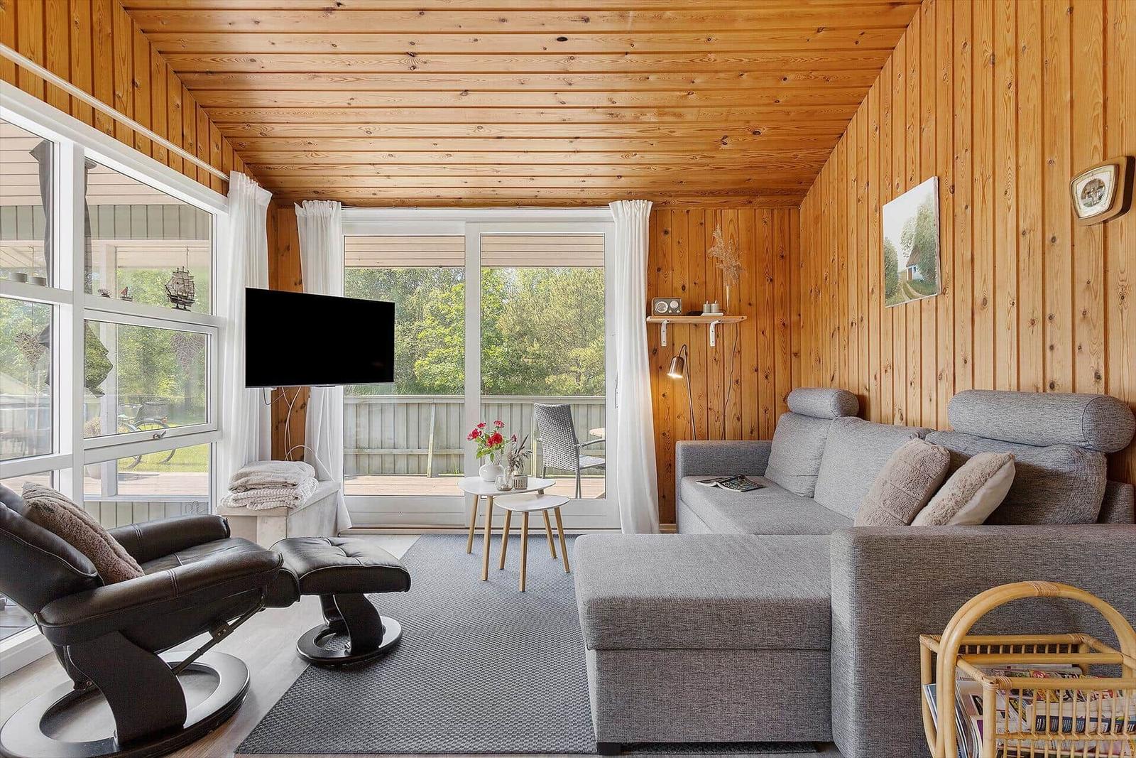 Living room with sofa, chair, TV, and large window to terrace.