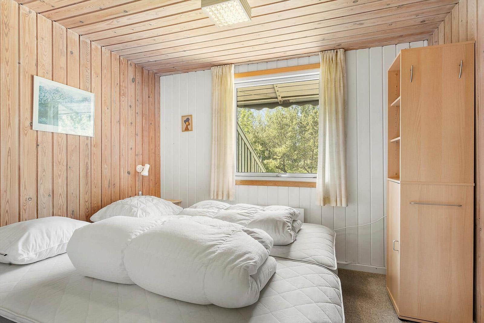 Bedroom with double bed, wooden walls, and window with view of trees.