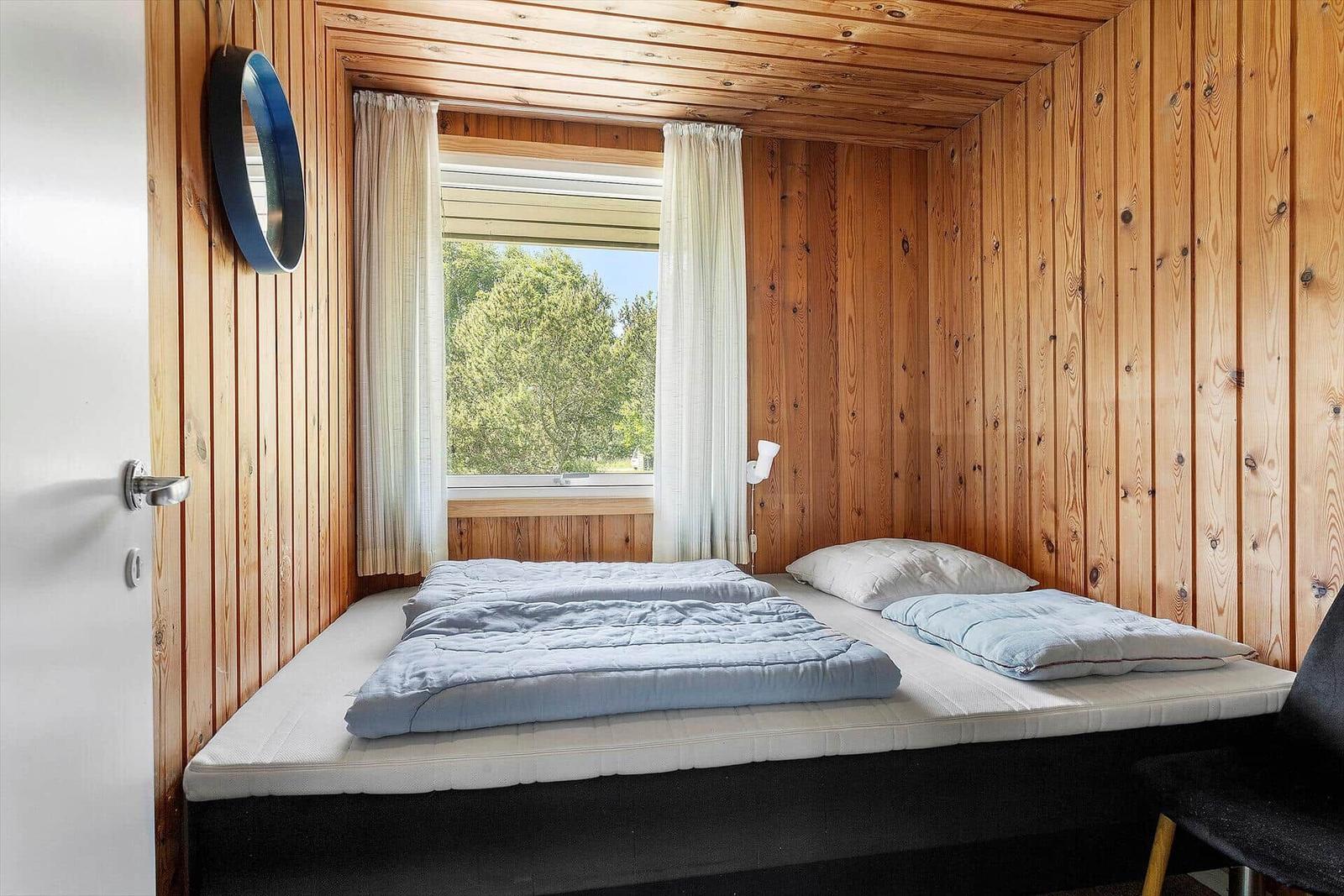 Bedroom with wooden walls, bed, and window with view of trees.