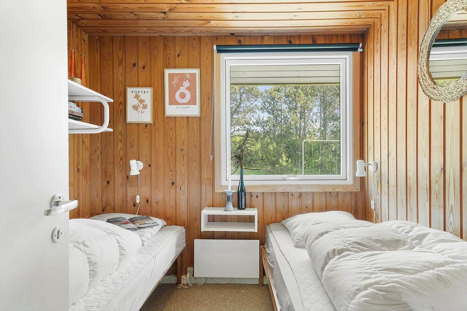 Two beds with white bedding, wooden walls, and window with view of forest.