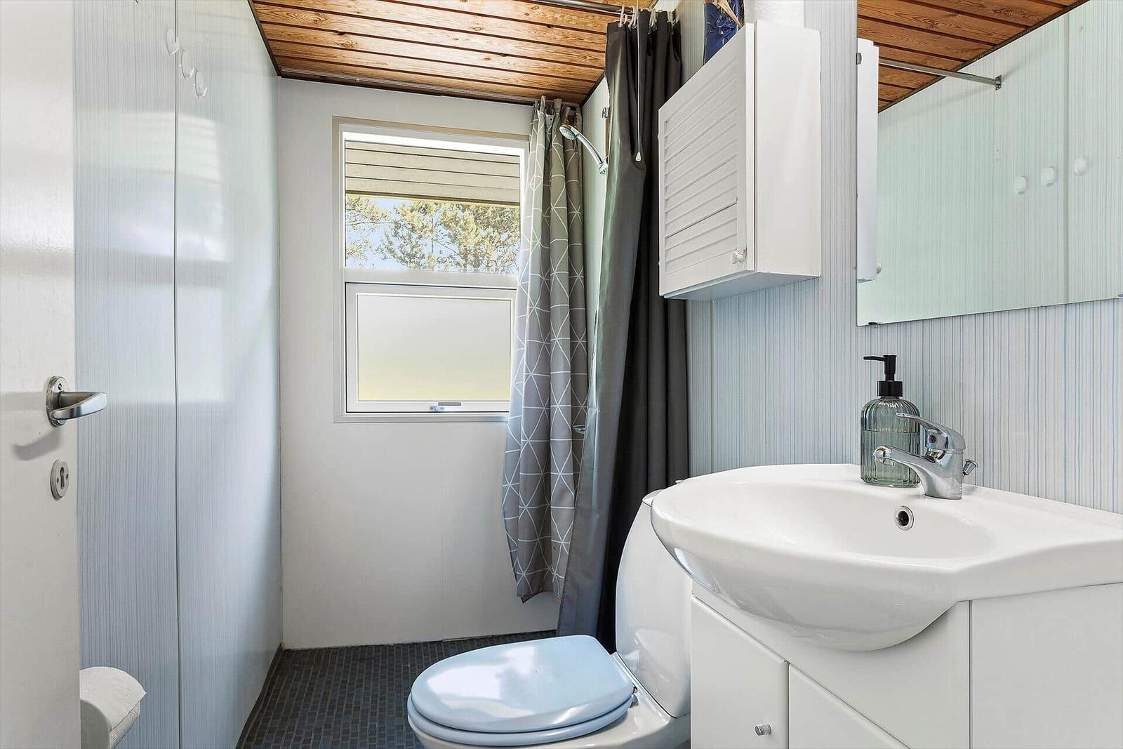 Bathroom with toilet, sink, and shower. Window with view outside.