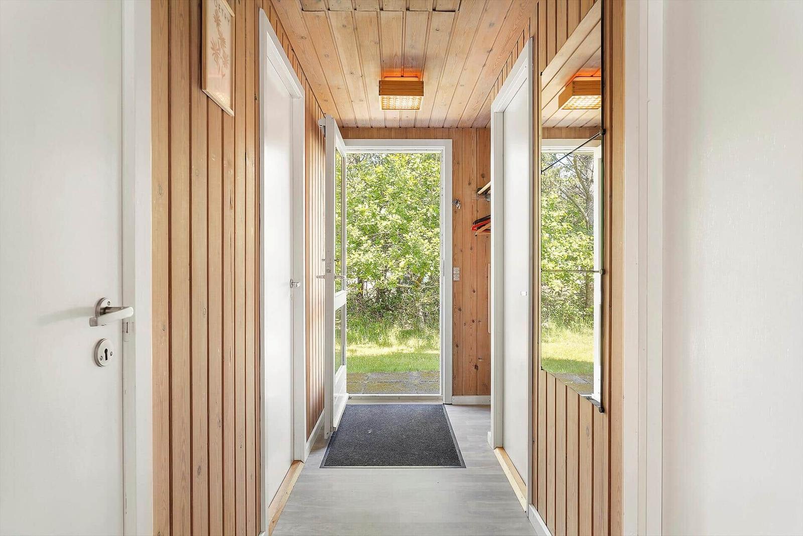 Hallway with wooden walls and door to green outdoor area.