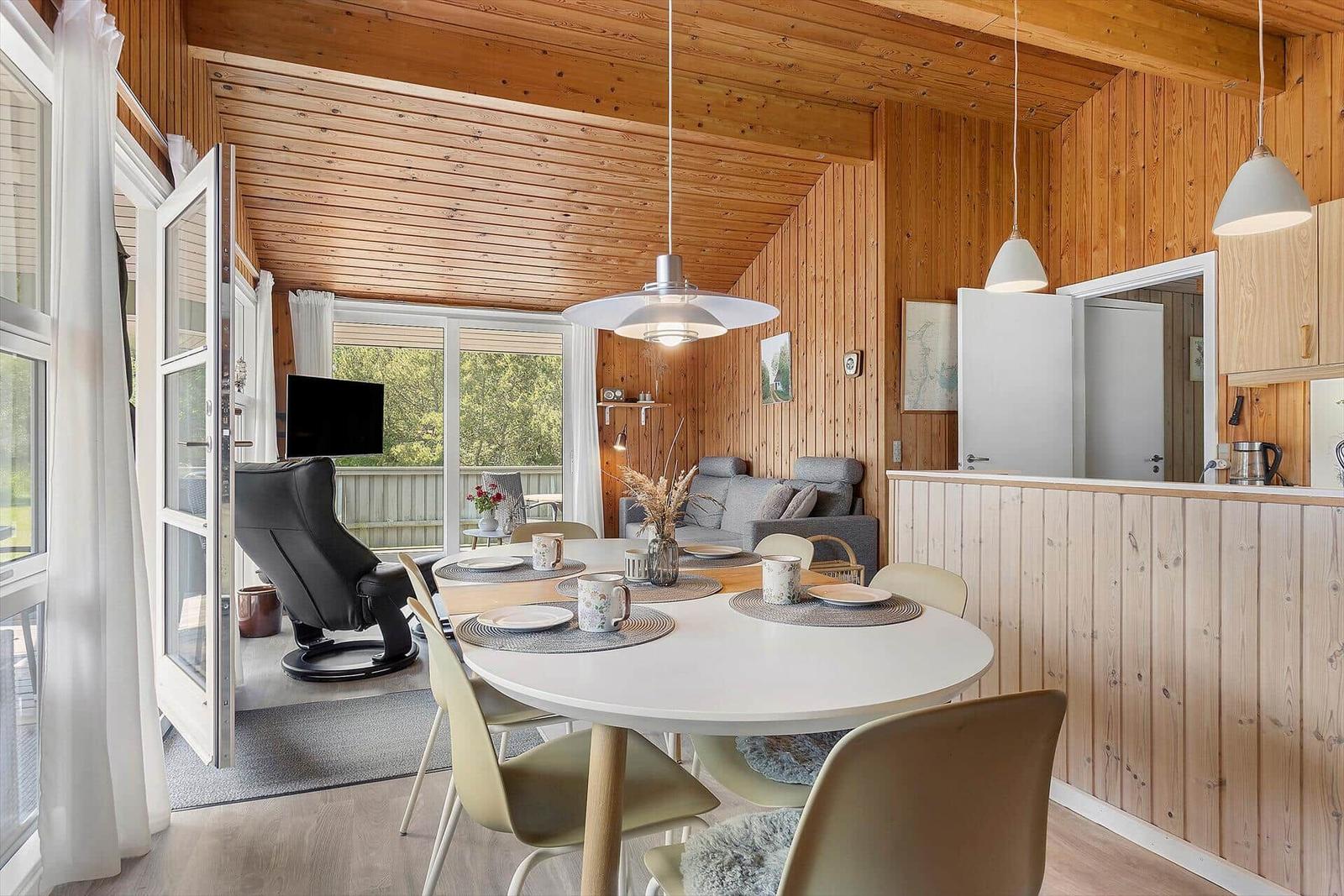 Dining room with round table and chairs, wooden walls, and windows to terrace.