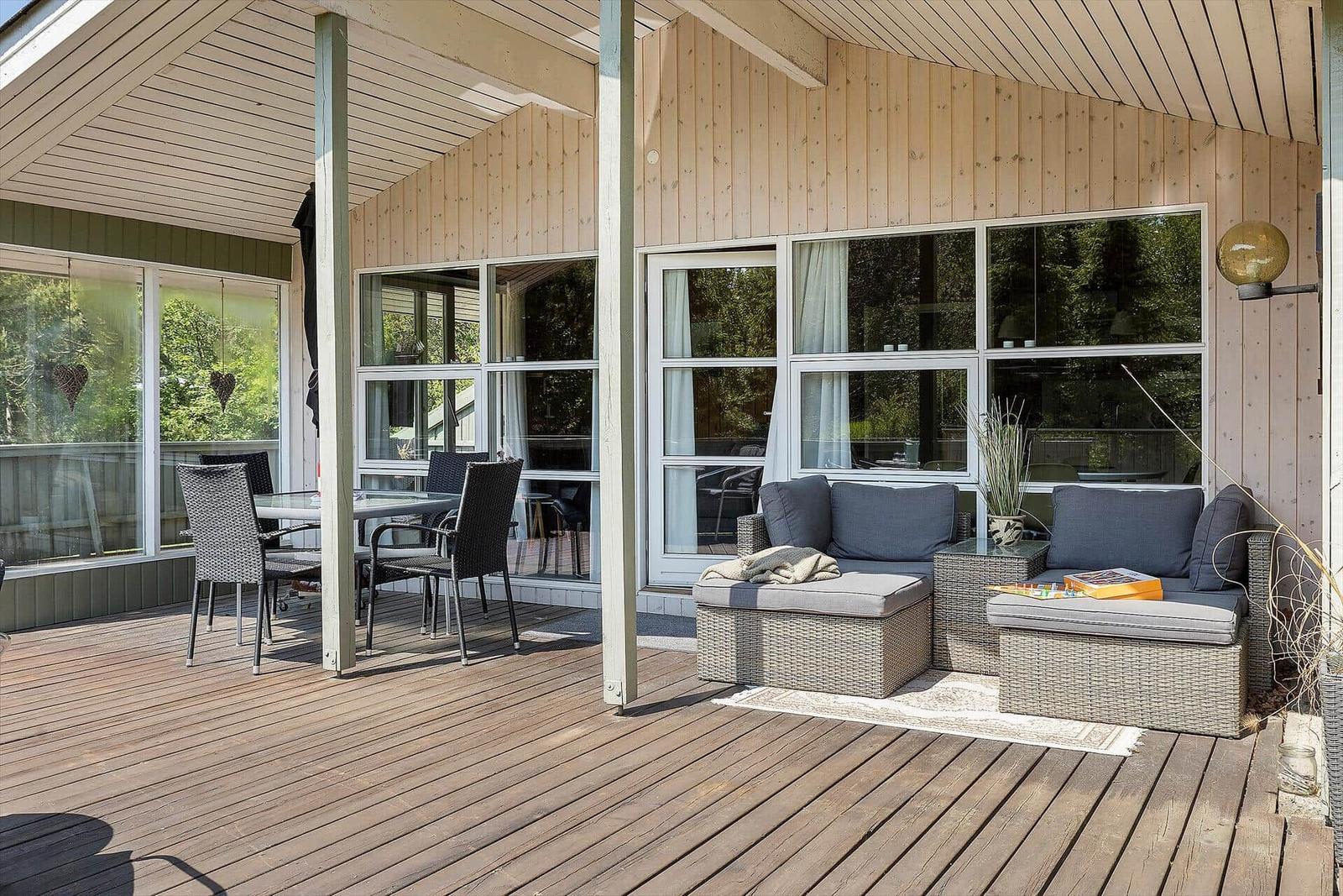 Deck with seating, dining table, and glass windows. Wooden walls and ceiling.