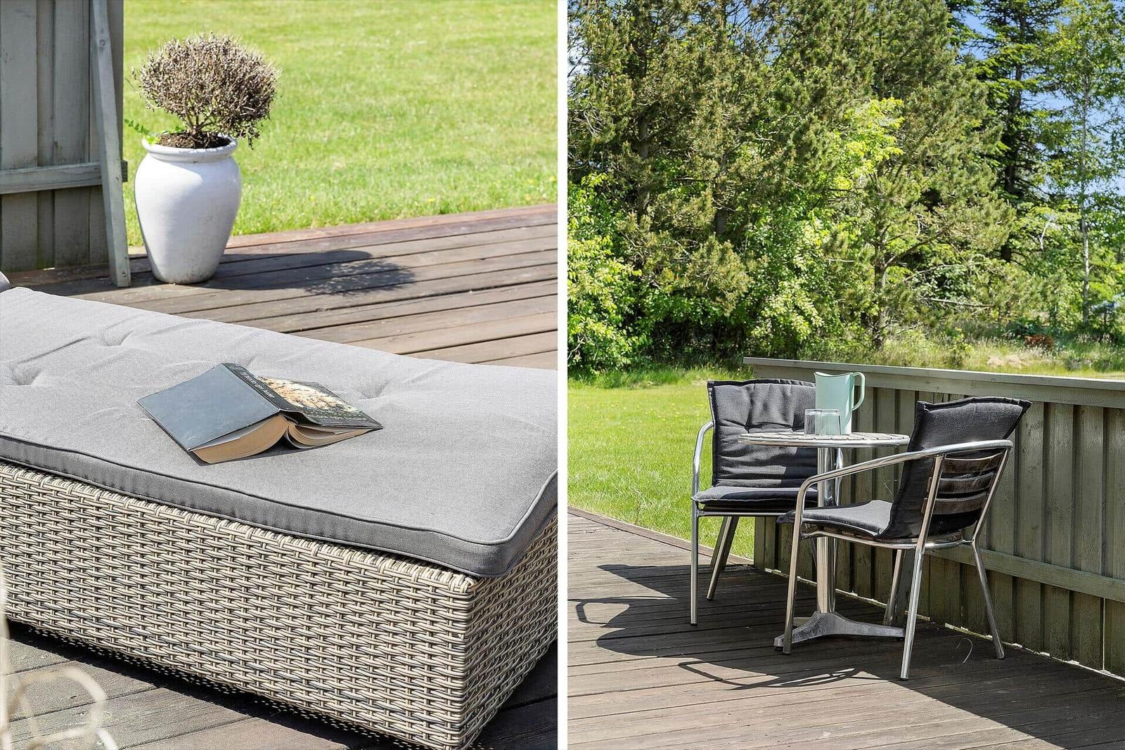 Deck with lounge and table for two. Greenery behind the railing.