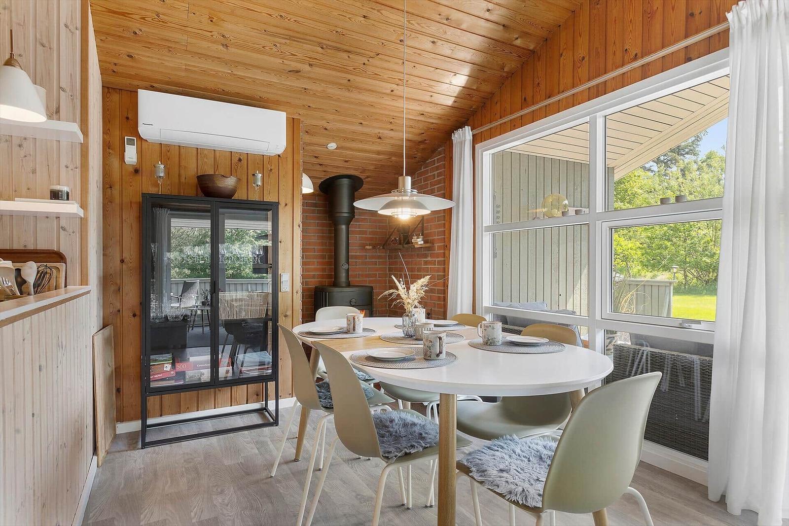 Dining area with round table and chairs, wooden walls, and large window.