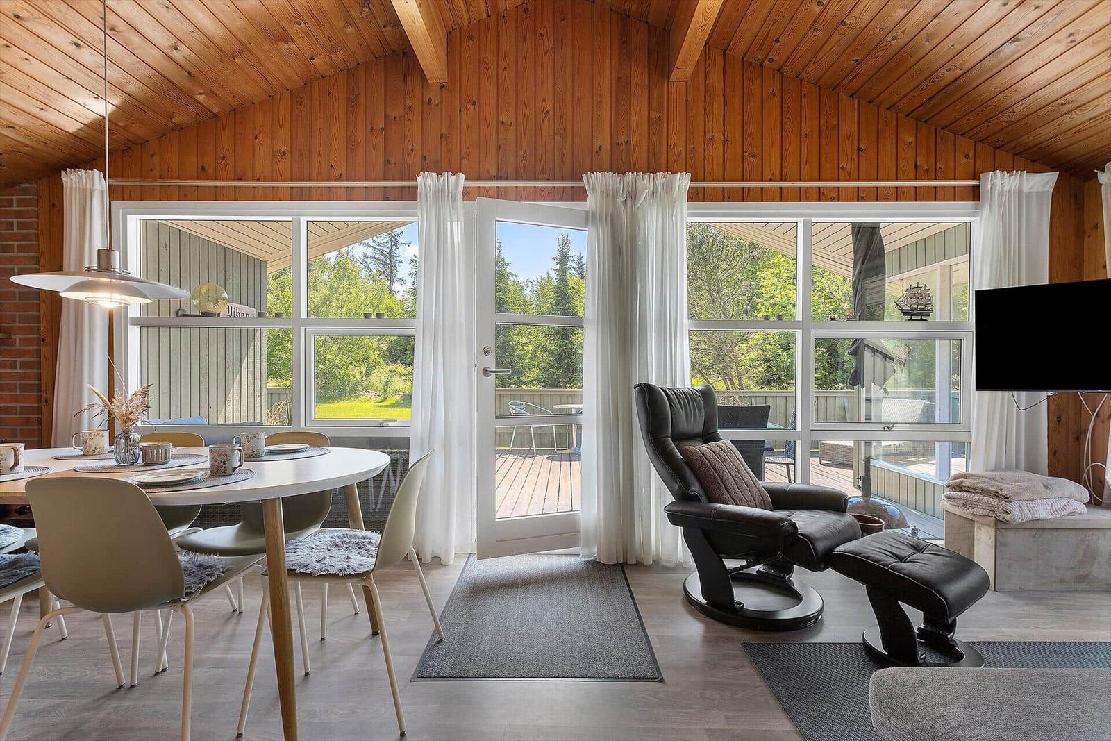 Living and dining area with wooden ceiling, windows, and seating.