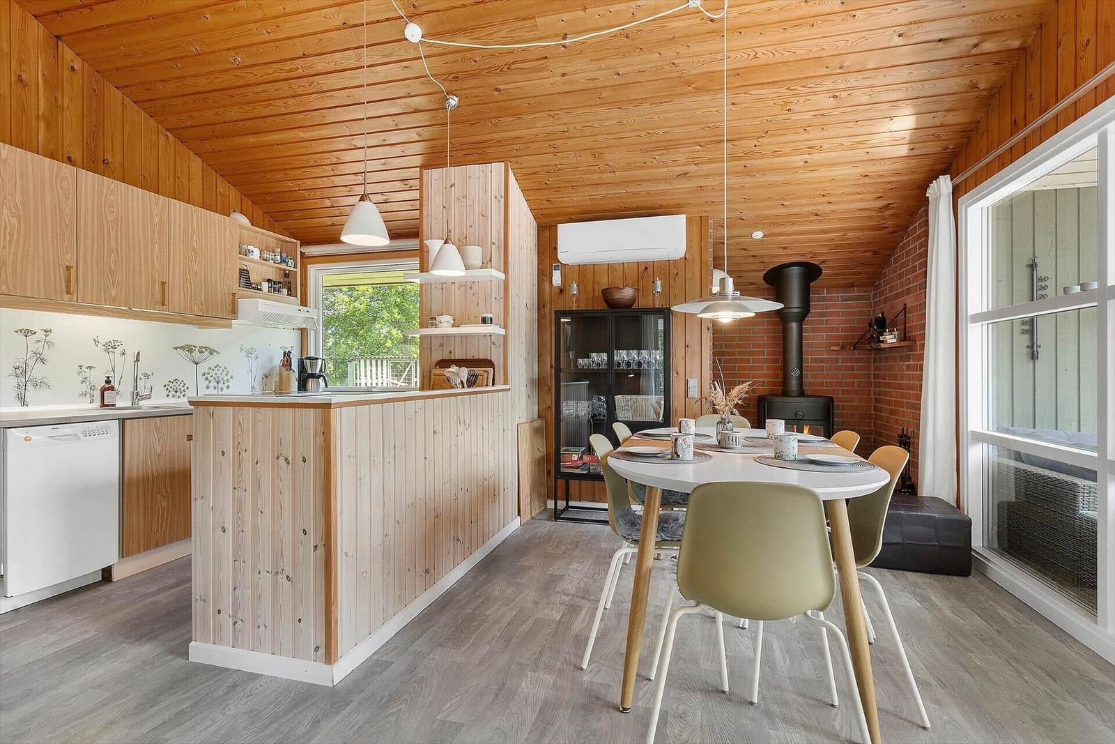Kitchen with dining area, wood walls and ceiling, dining table with chairs, fireplace and windows.