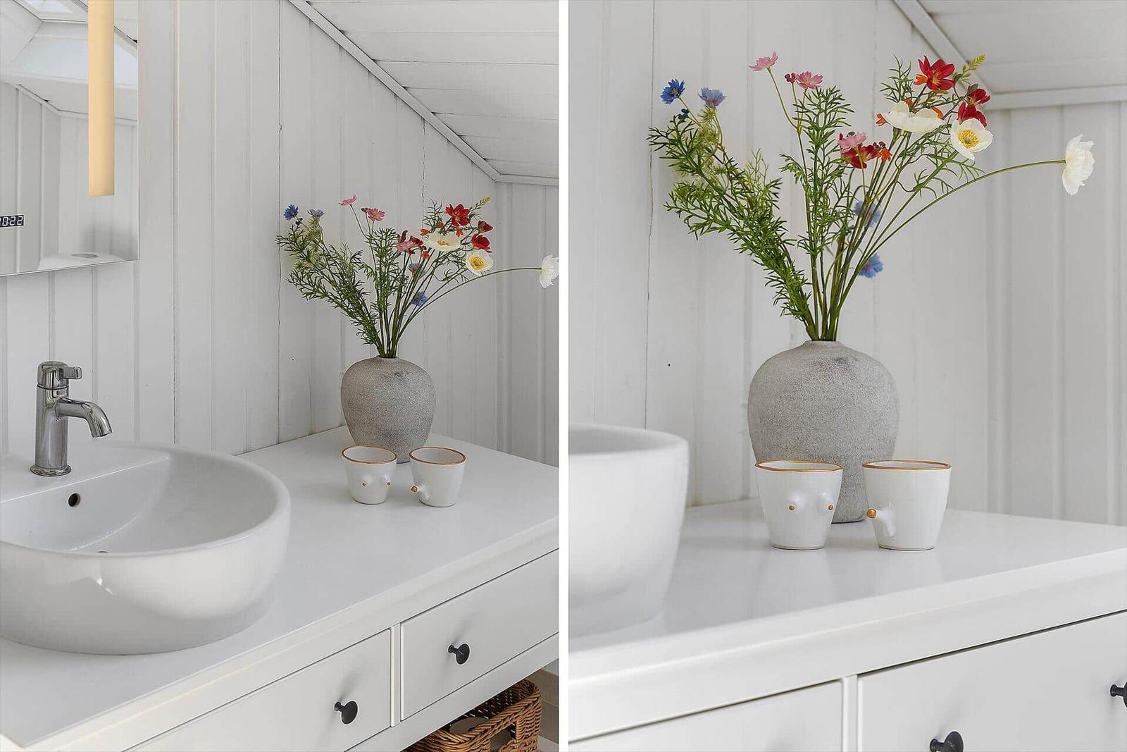 Badezimmer mit Waschbecken, Vase und zwei Tassen auf weißem Schrank.