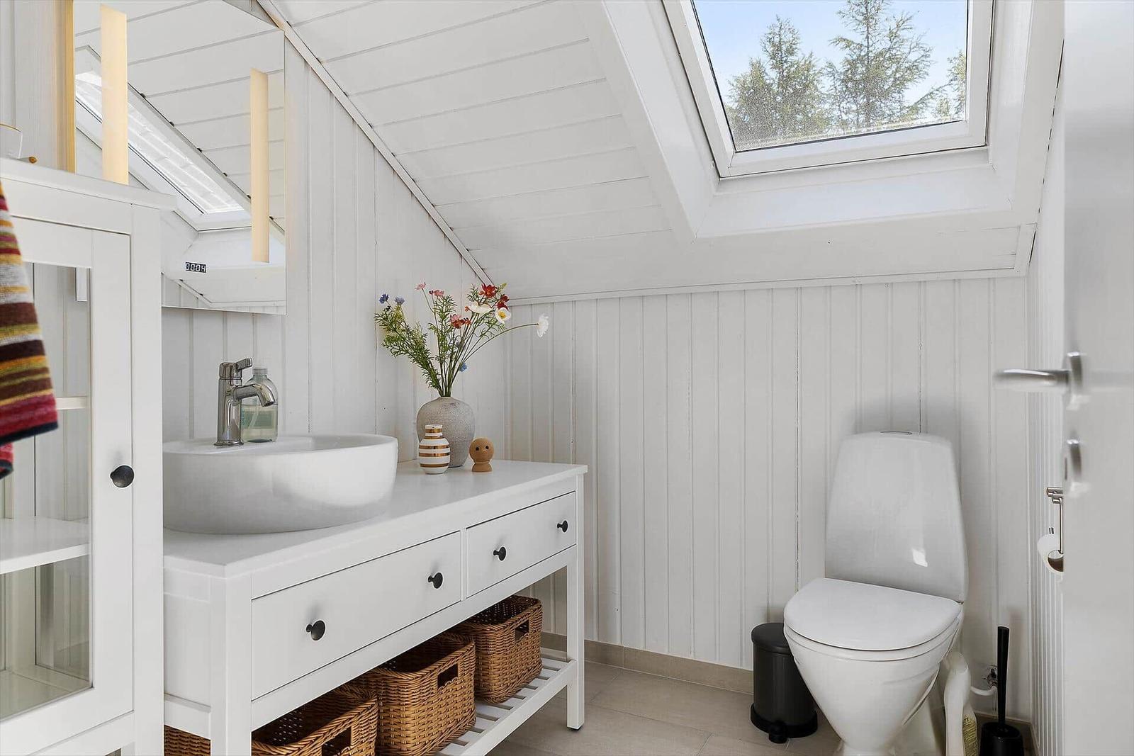 Badezimmer mit Waschtisch, Toilette und Dachfenster. Weiße Wände und Holzdecke.