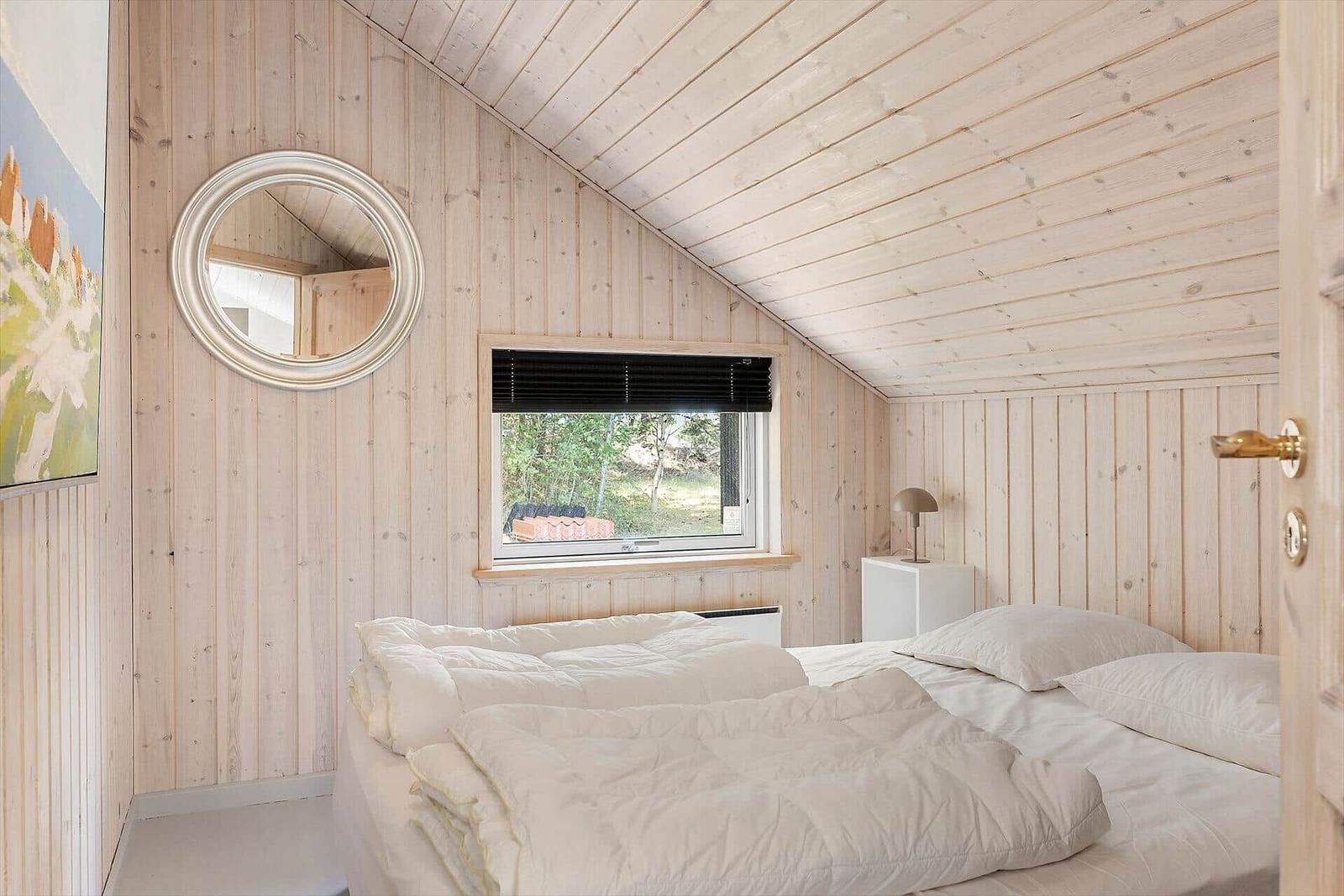 Schlafzimmer mit Holzwand, Bett und Fenster mit Blick nach draußen.
