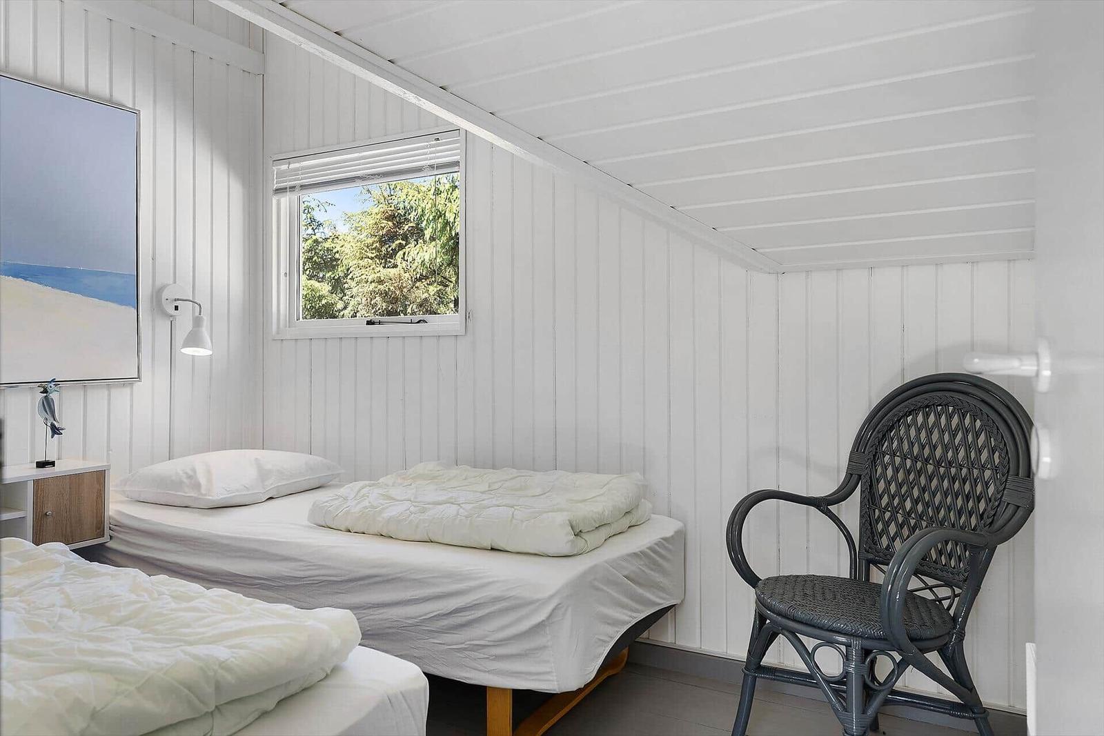 Zimmer mit zwei Betten, Stuhl und Fenster mit Blick auf Bäume.