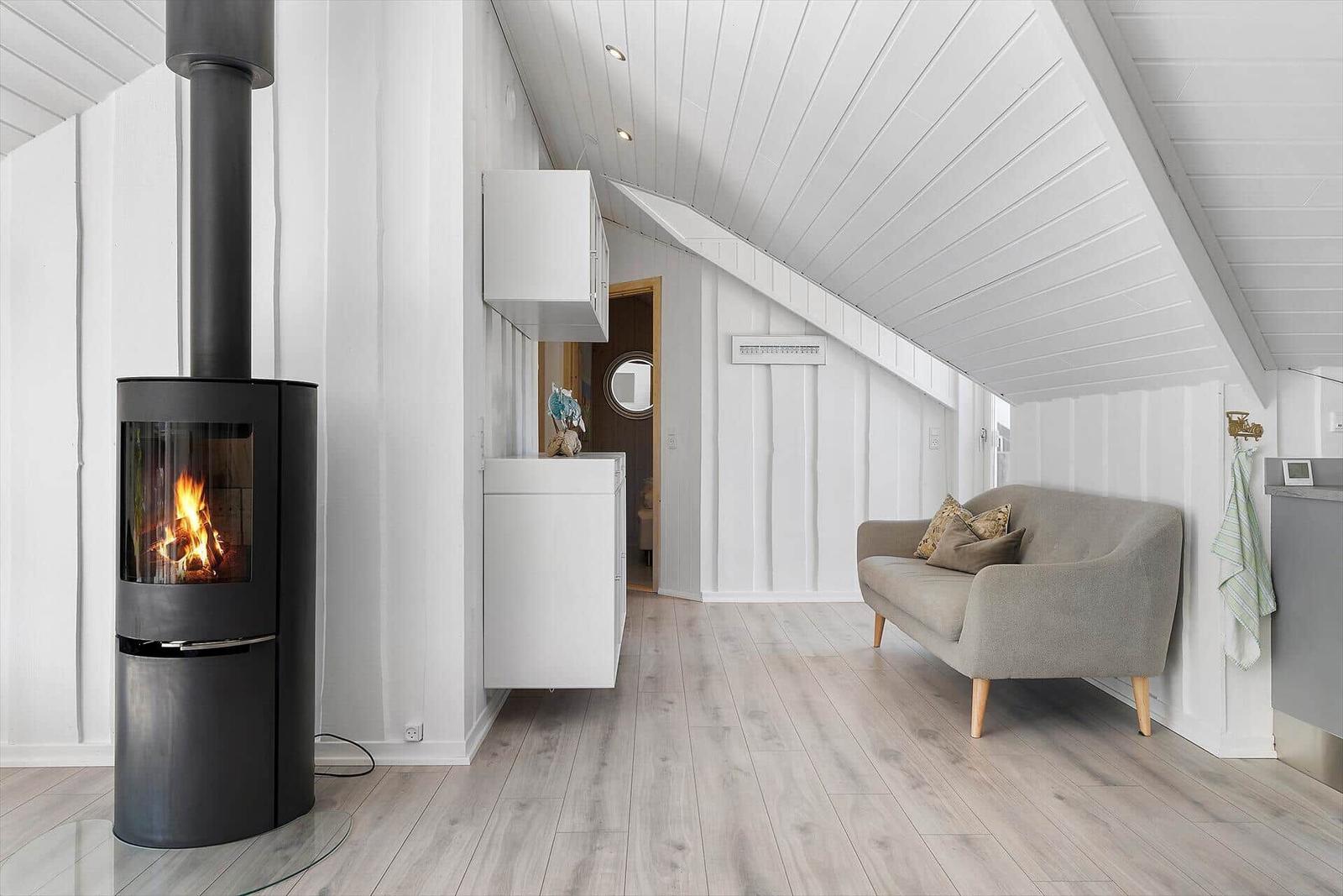 Wohnraum mit Kamin, Sofa und weißen Wänden unter Dachschrägen.