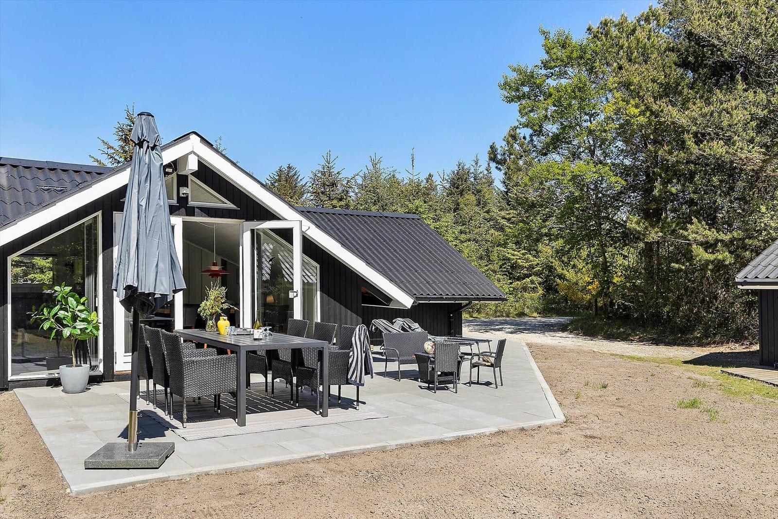 Modernes Haus mit großem Außenbereich, Tisch, Stühlen und Sonnenschirm.