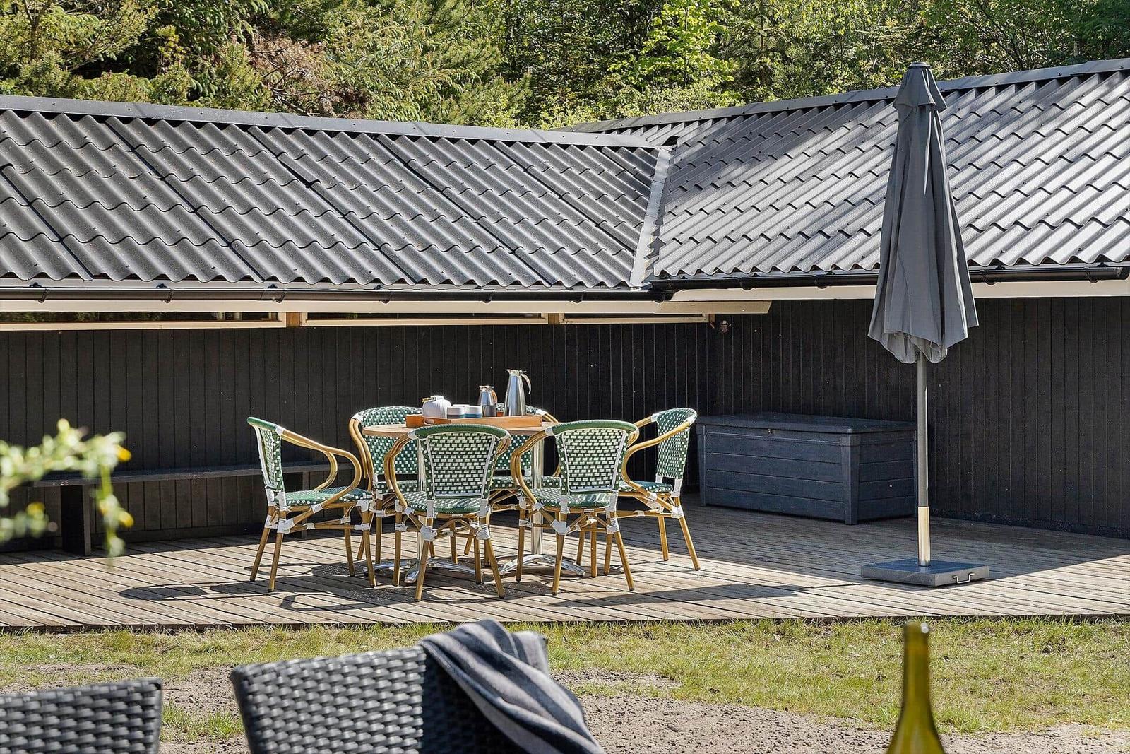 Terrasse mit Tisch, Stühlen und Sonnenschirm vor schwarzem Holzhaus