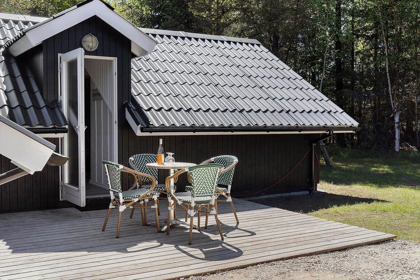 Hütte mit Terrasse, Tisch und vier Stühlen, umgeben von Wald.