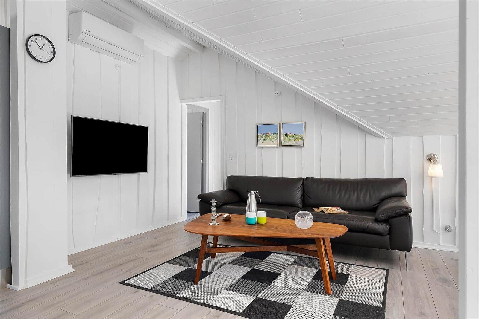 Wohnzimmer mit schwarzem Sofa, Holztisch und Fernseher an weißer Wand.