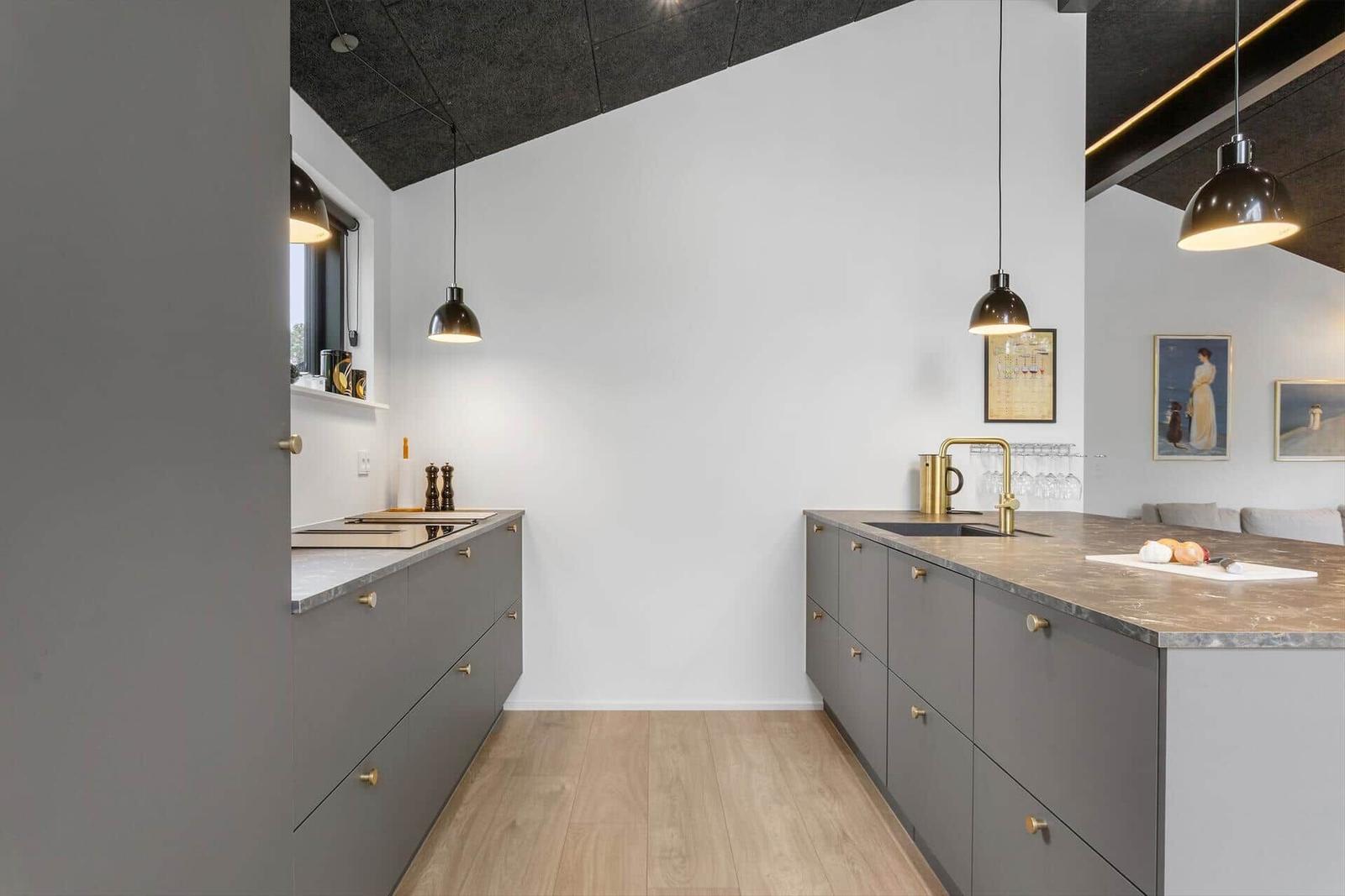 Moderne Küche mit grauen Schränken, Steinarbeitsplatte und hängenden Lampen.