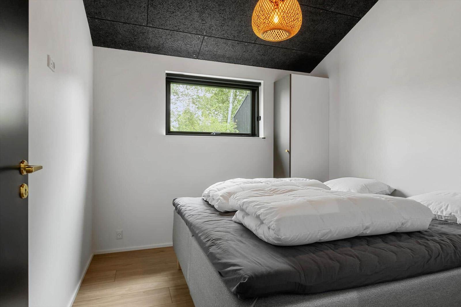 Schlafzimmer mit Bett, Fenster und Deckenleuchte.