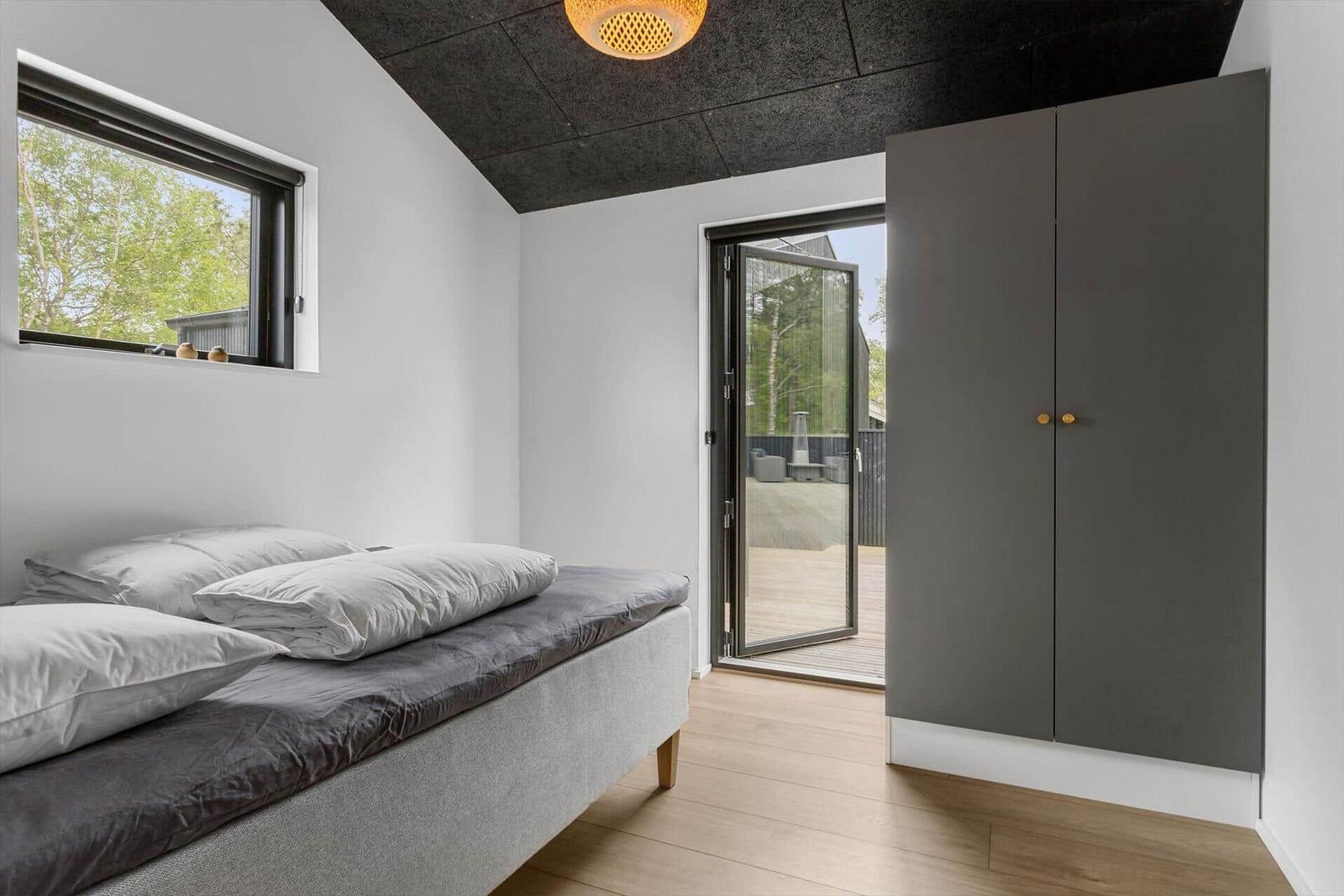 Schlafzimmer mit Bett, Kleiderschrank und Balkontür. Holzboden und Fenster mit Blick auf Grün.