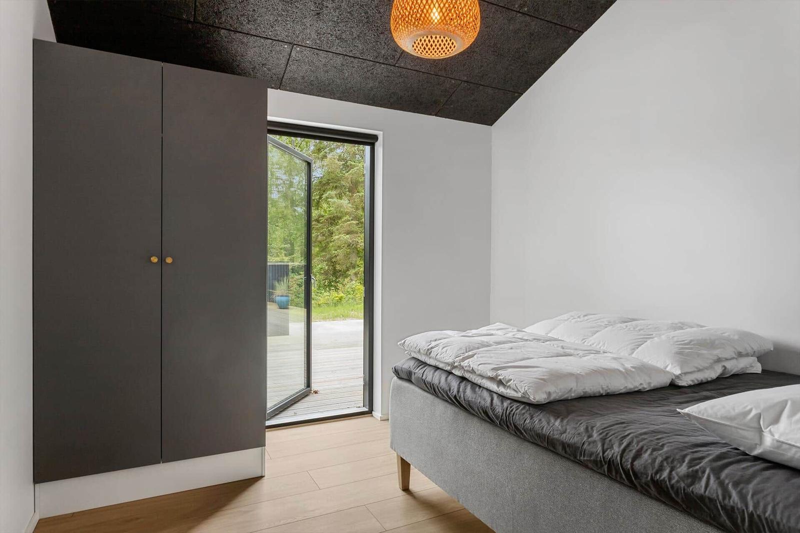 Schlafzimmer mit Bett, Kleiderschrank und Glastür zum Garten.