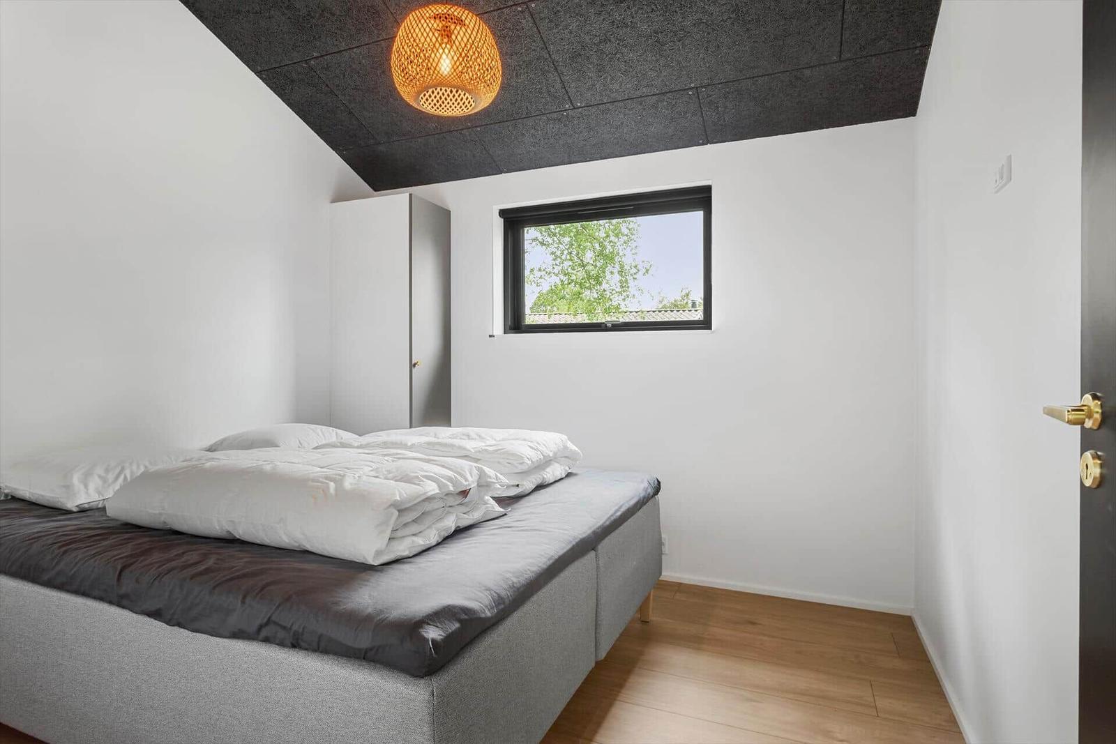 Schlafzimmer mit Bett, Fenster und Deckenleuchte.