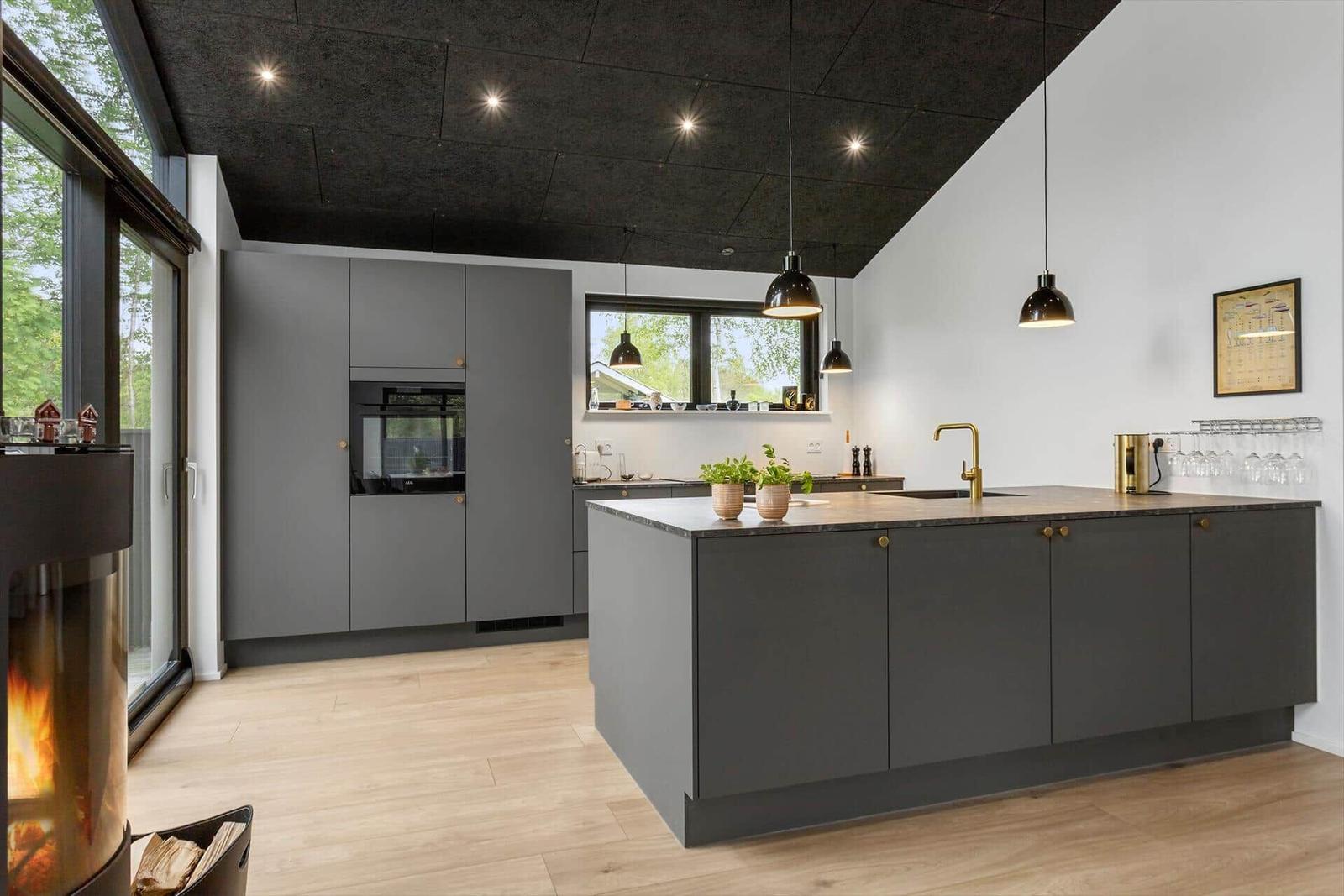 Moderne Küche mit grauen Schränken, Holzboden und schwarzer Decke. Feuer im Kamin.