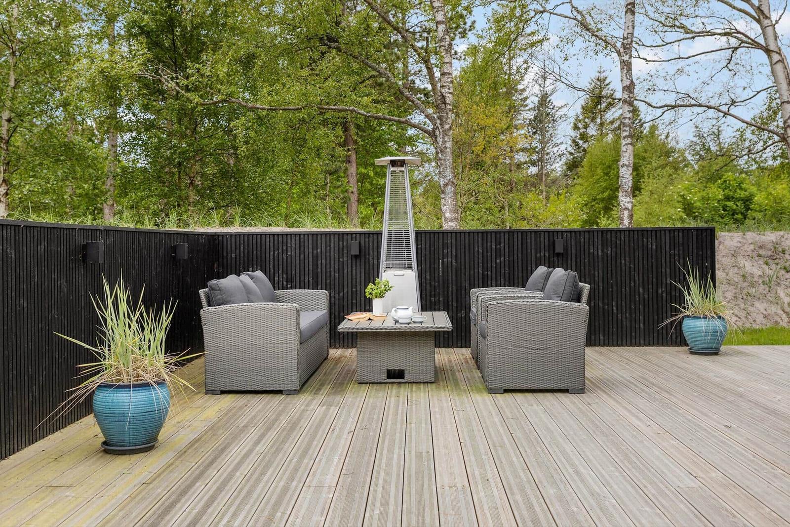 Terrasse mit Sitzgruppe, Grill und Pflanzen. Holzdecke und schwarze Wand.